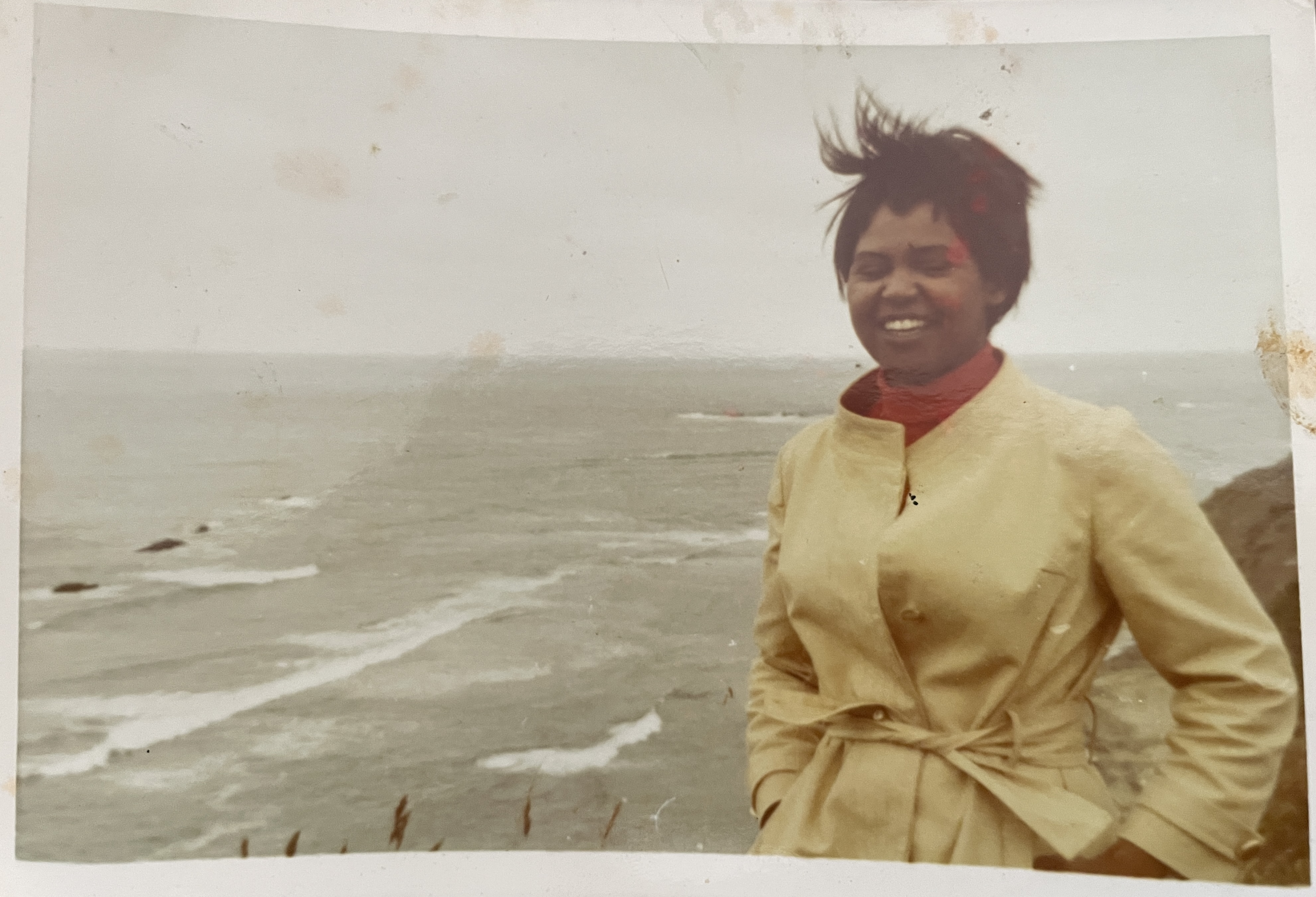 A woman smiling by the ocean in a golden coat — the original Salvaged Beauty